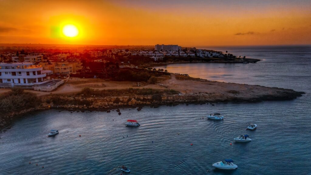 Golden sunset over the calm waters of Golden Coast in Protaras, Cyprus, with boats gently bobbing in the bay.