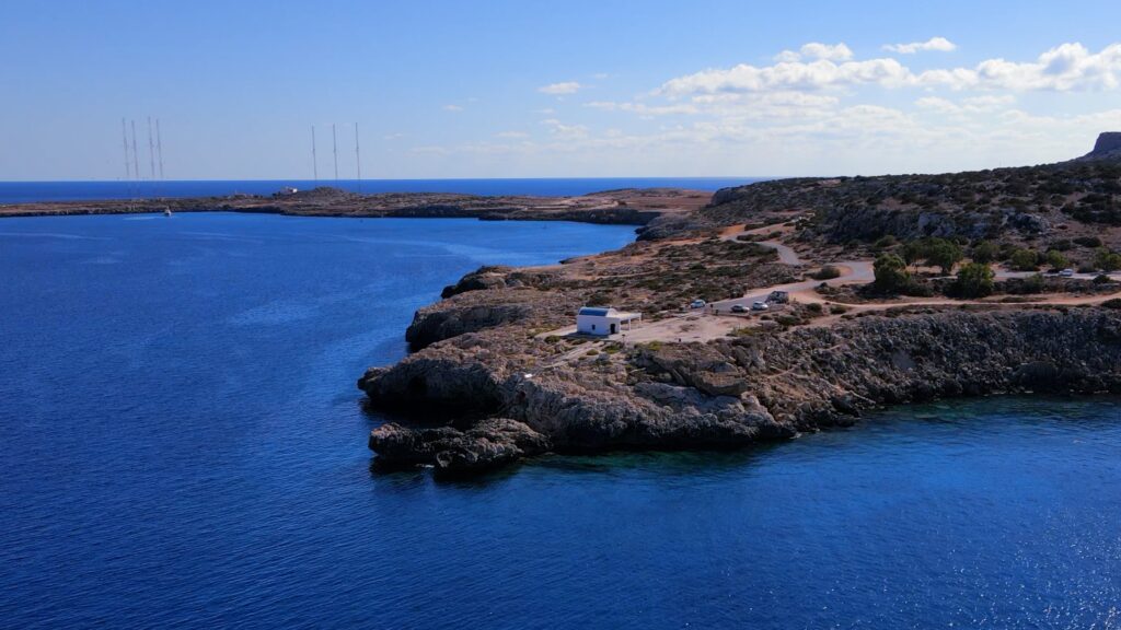 Aerial shot of Ayioi Anargyroi Chapel perched on the cliff, flanked by two natural bays with sparkling blue waters.