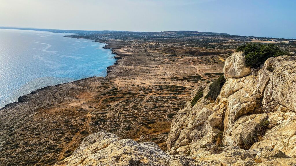 Aerial perspective of Cavo Greco peninsula showcasing the rugged cliffs and clear blue sea.