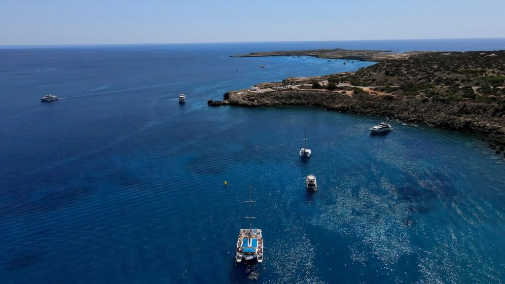 Drone photo capturing the meeting point of Konnos Bay and Cavo Greco peninsula, dotted with boats.