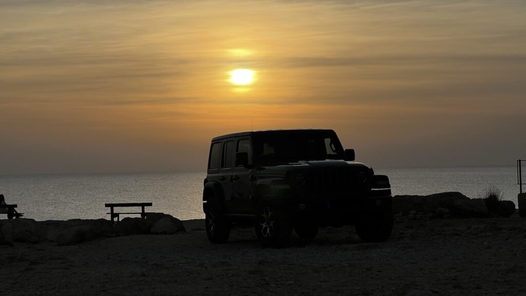 Jeep Wrangler parked near the sea caves of Cape Greco, bathed in the glow of the setting sun.