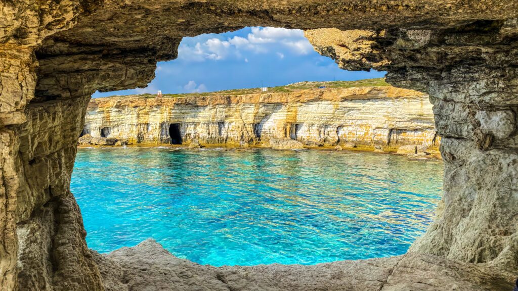 A picturesque view of the Sea Caves at Cape Greco, showcasing the crystal clear blue sea and the uniquely sculpted other section of the caves, captured from a vantage point.