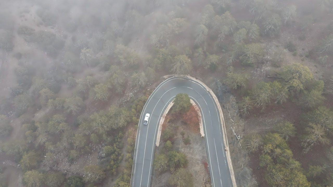 Aerial view of a winding road cutting through the foggy Troodos mountains, embodying the serene mountain experiences in Cyprus.