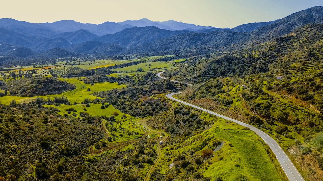Aerial view of a winding road cutting through the verdant valleys of Cyprus's generic mountain terrain.