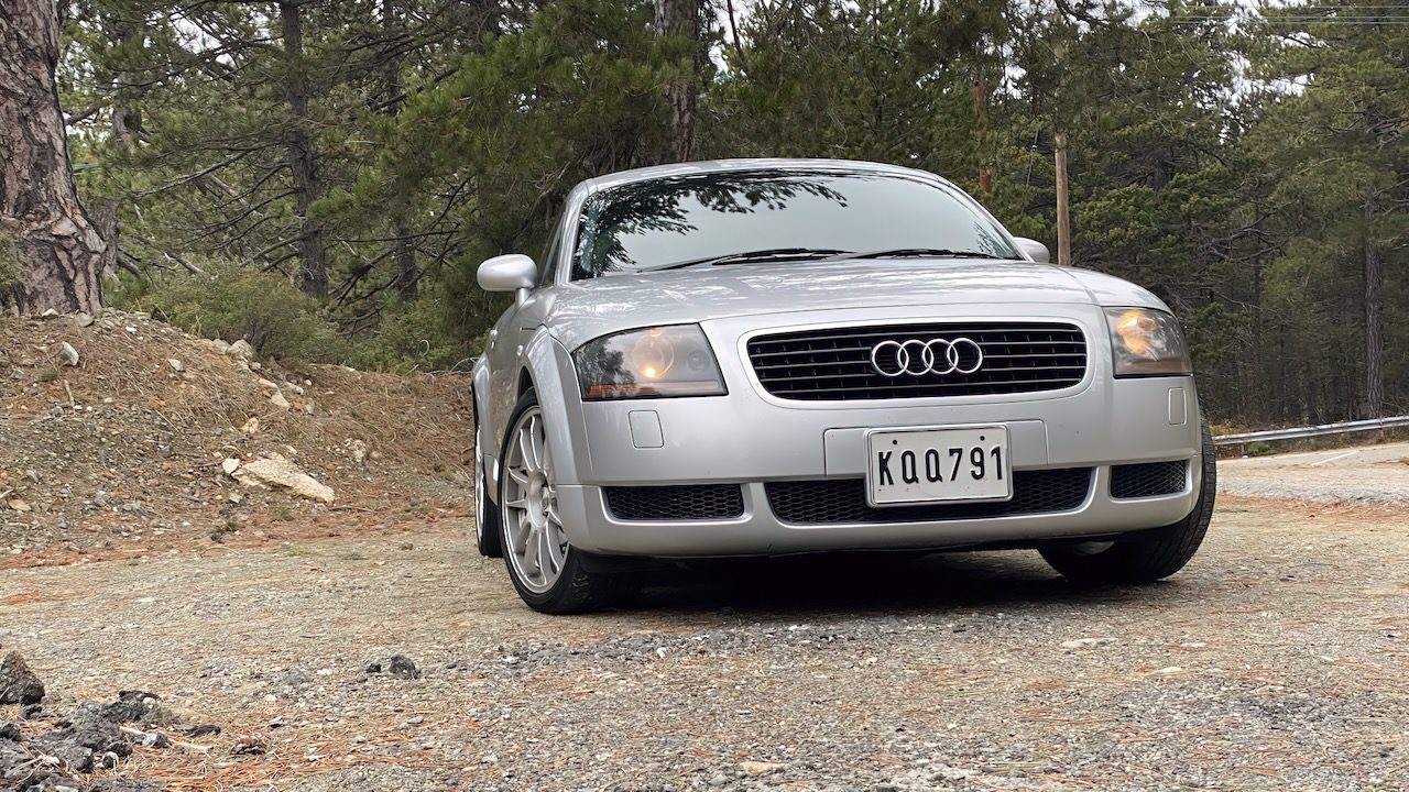 A silver Audi TT parked on a gravel road amidst the Troodos mountain range, ready for a mountain driving experience.