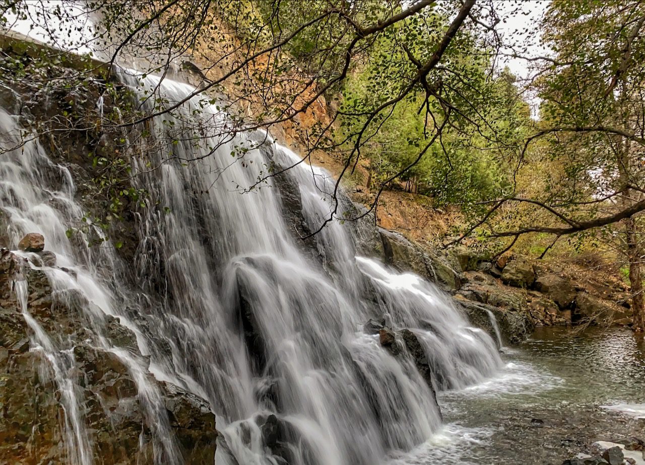 Water cascades down the Xyliatos Dam Waterfall in Cyprus, surrounded by the rich flora and natural beauty of the island.