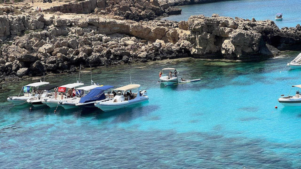 Boats anchored in the crystal clear turquoise waters of Cavo Greco, Blue Lagoon in Cyprus, during summer showcasing the serene sea temperature of the Mediterranean Sea.