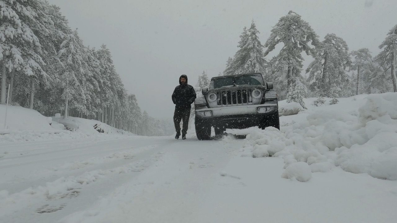 A solitary figure and a rugged Jeep stand resilient amidst the snow-covered landscape of the Troodos Mountains, a testament to the challenging weather conditions in Cyprus during winter.