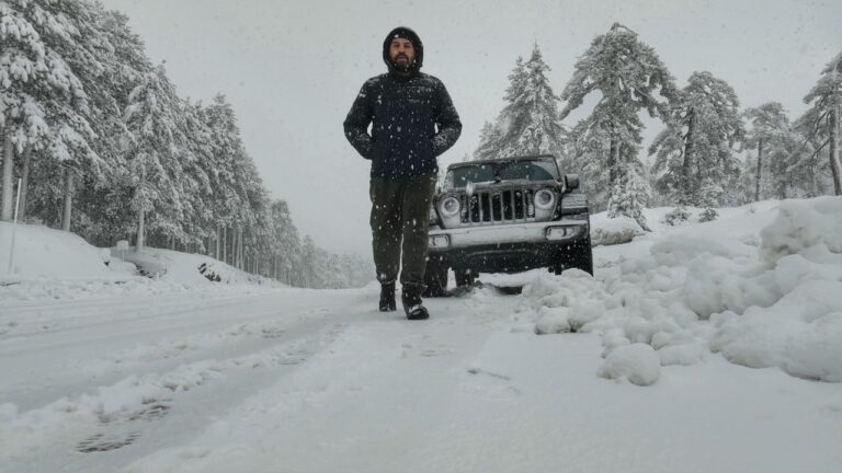 Man standing on a snow-covered road in the Troodos Mountains with a Jeep in the background, illustrating winter exploration in Cyprus.