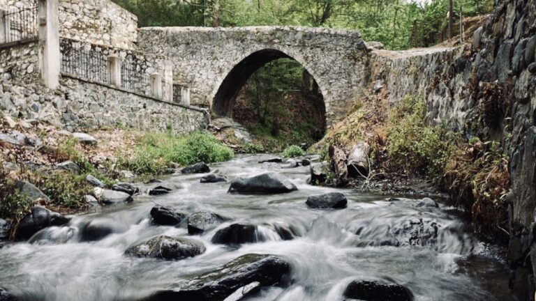 Historic Kalopanagiotis Venetian Bridge over a flowing river surrounded by lush greenery in the Troodos Mountains.