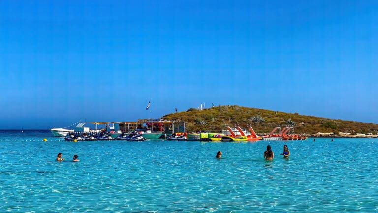 Clear turquoise waters and beachgoers enjoying water sports at Nissi Beach, highlighting the area’s appeal as a tourist destination.